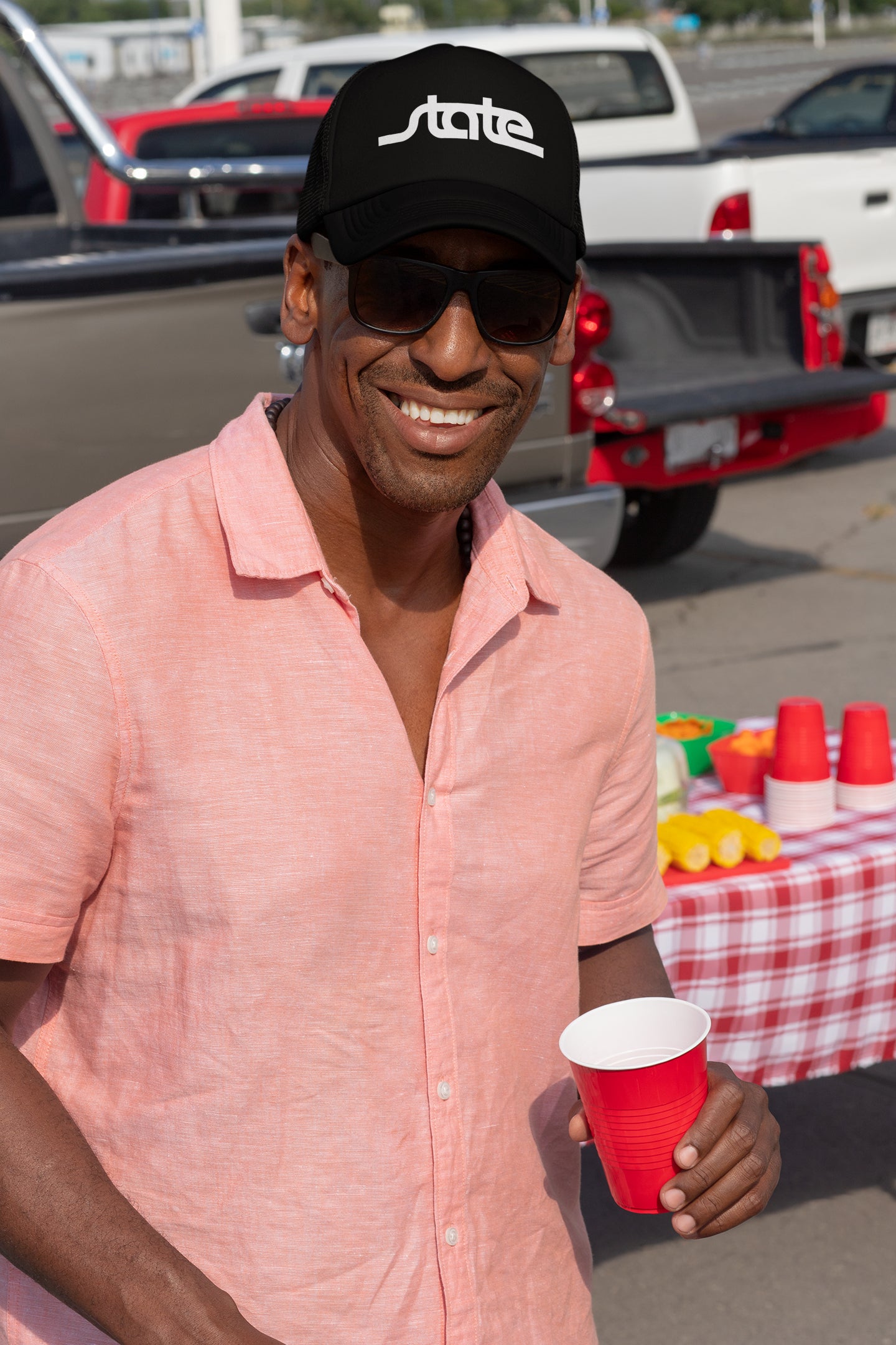 Handsome man smiling wearing Row One Brand merch, a retro script "state" snapback hat while tailgating on gameday.