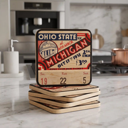 A stack of square wooden coasters featuring a Row One Brand 1931 vintage Ohio State vs. Michigan football ticket design, displayed on a white marble kitchen countertop with a blurred kitchen background.