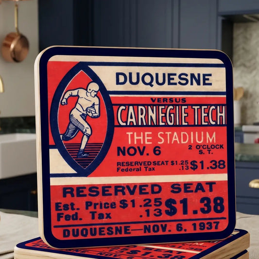 A square decorative reusable birch wood coaster featuring a vintage 1937 football ticket design for Duquesne versus Carnegie Tech at The Stadium, with bold red, cream, and navy graphics and text. The coaster is photographed standing on top of similar signs in a kitchen-like setting. Elements of image generated by AI