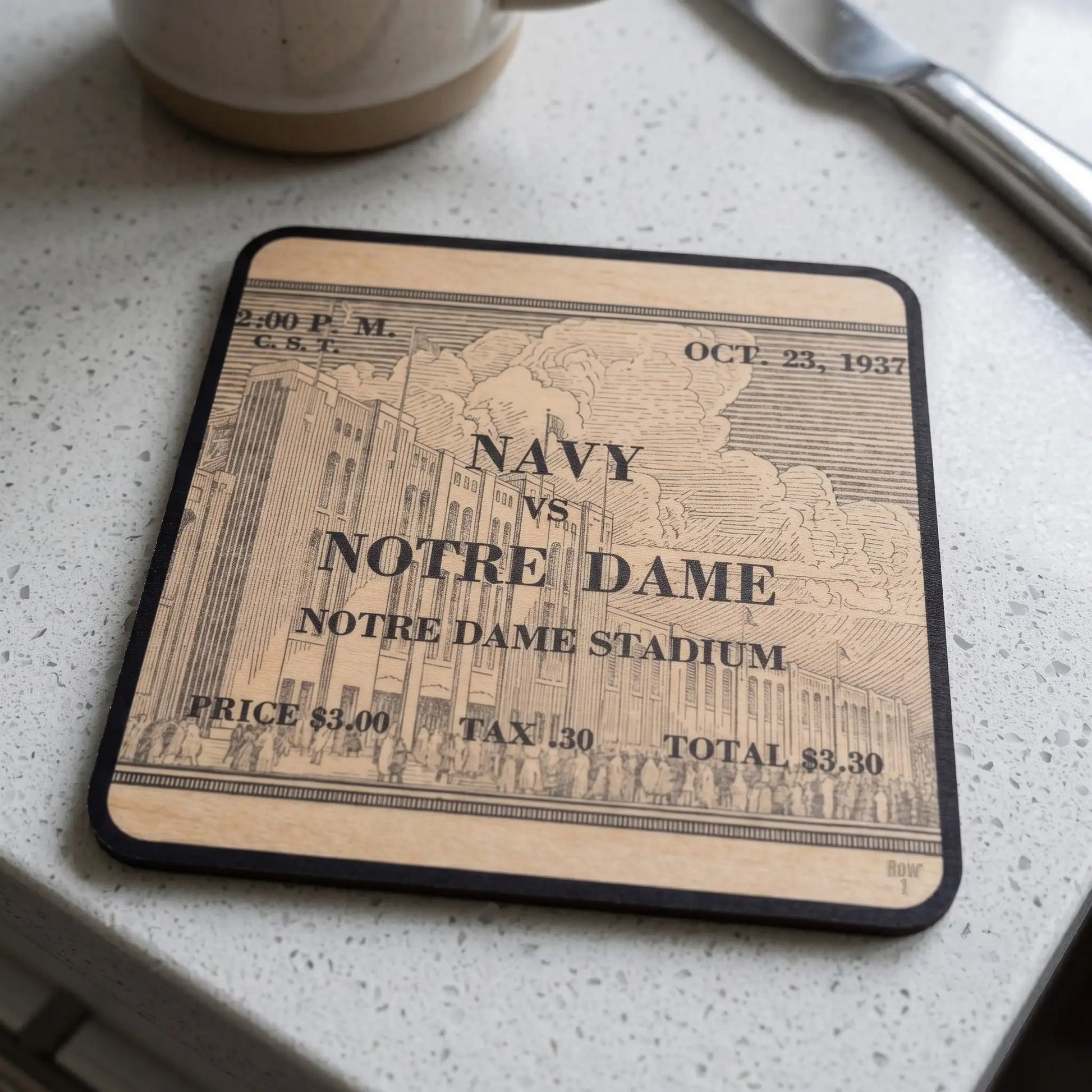 A Row One Brand square wooden coaster with a black border and Row 1 trademark in lower corner of wood coaster featuring a vintage college football ticket design for a 1937 Navy vs. Notre Dame game, resting on a speckled white countertop.