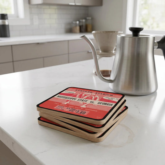 A stack of Row One Brand Row 1™ square wooden coasters with red and white Mississippi State vs. Georgia collegiate football ticket stub print and Row 1™ trademark in lower corner, birch wood coasters sit on a white kitchen countertop, with a stainless steel gooseneck kettle in the background.