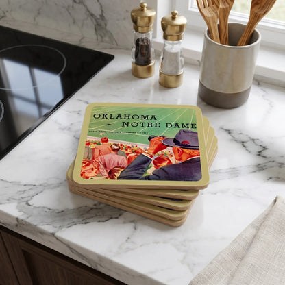 A stack of square coasters with rounded corners sits on a white marble kitchen countertop. The coasters have a gold border and a printed design featuring Oklahoma Notre Dame football players in a stadium, with the text 'OKLAHOMA NOTRE DAME' at the top, date of game, and vintage football stadium art.
