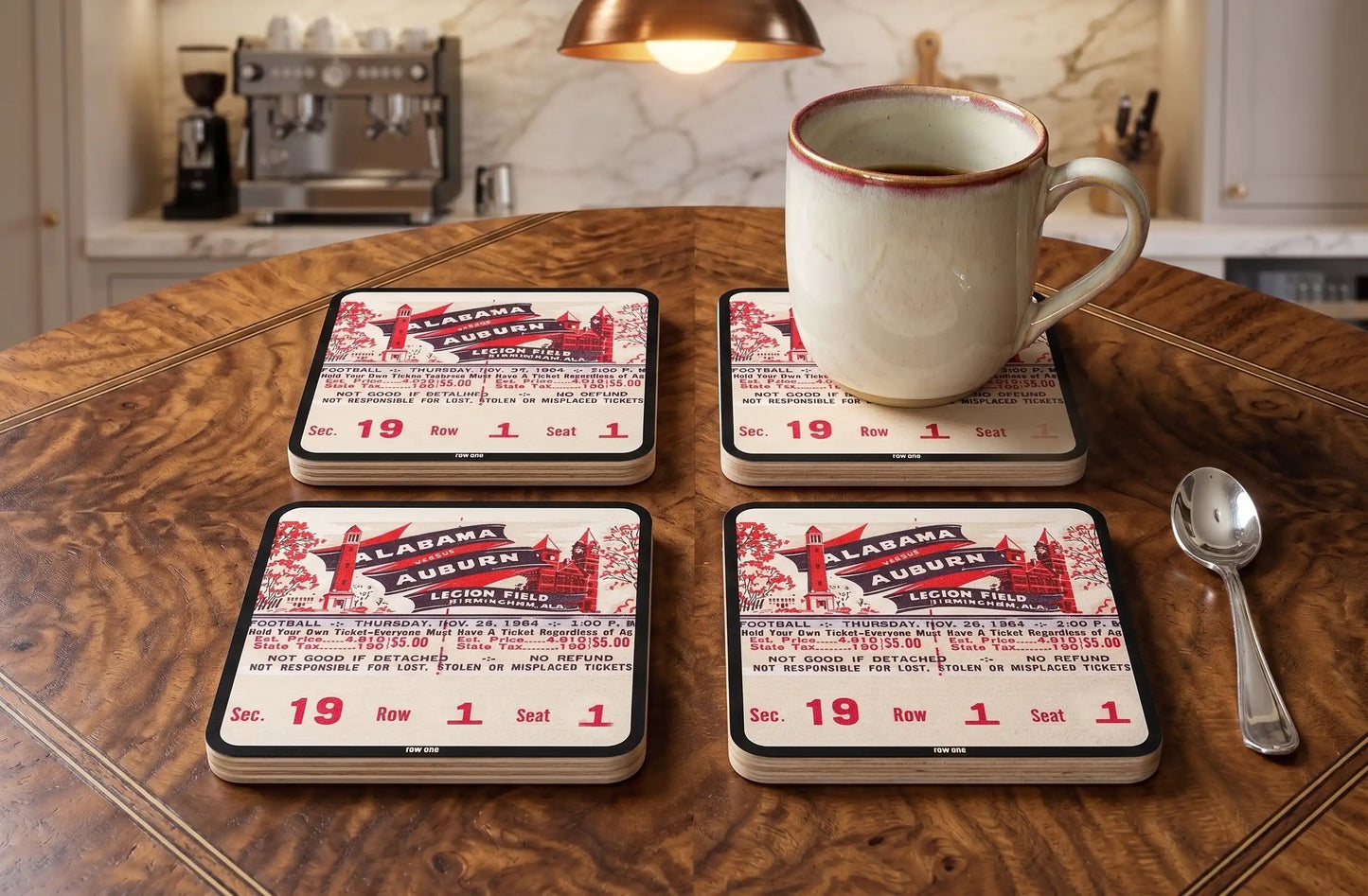 Four Row One Brand vintage college football ticket drink coasters with 1954 Alabama-Auburn football ticket design and Row One™ trademark in lower center of border laying on kitchen table with cup of coffee