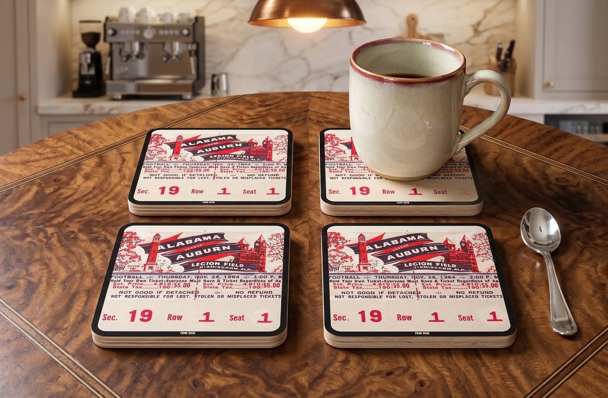 Four Row One Brand vintage college football ticket drink coasters with 1954 Alabama-Auburn football ticket design and Row One™ trademark in lower center of border laying on kitchen table with cup of coffee