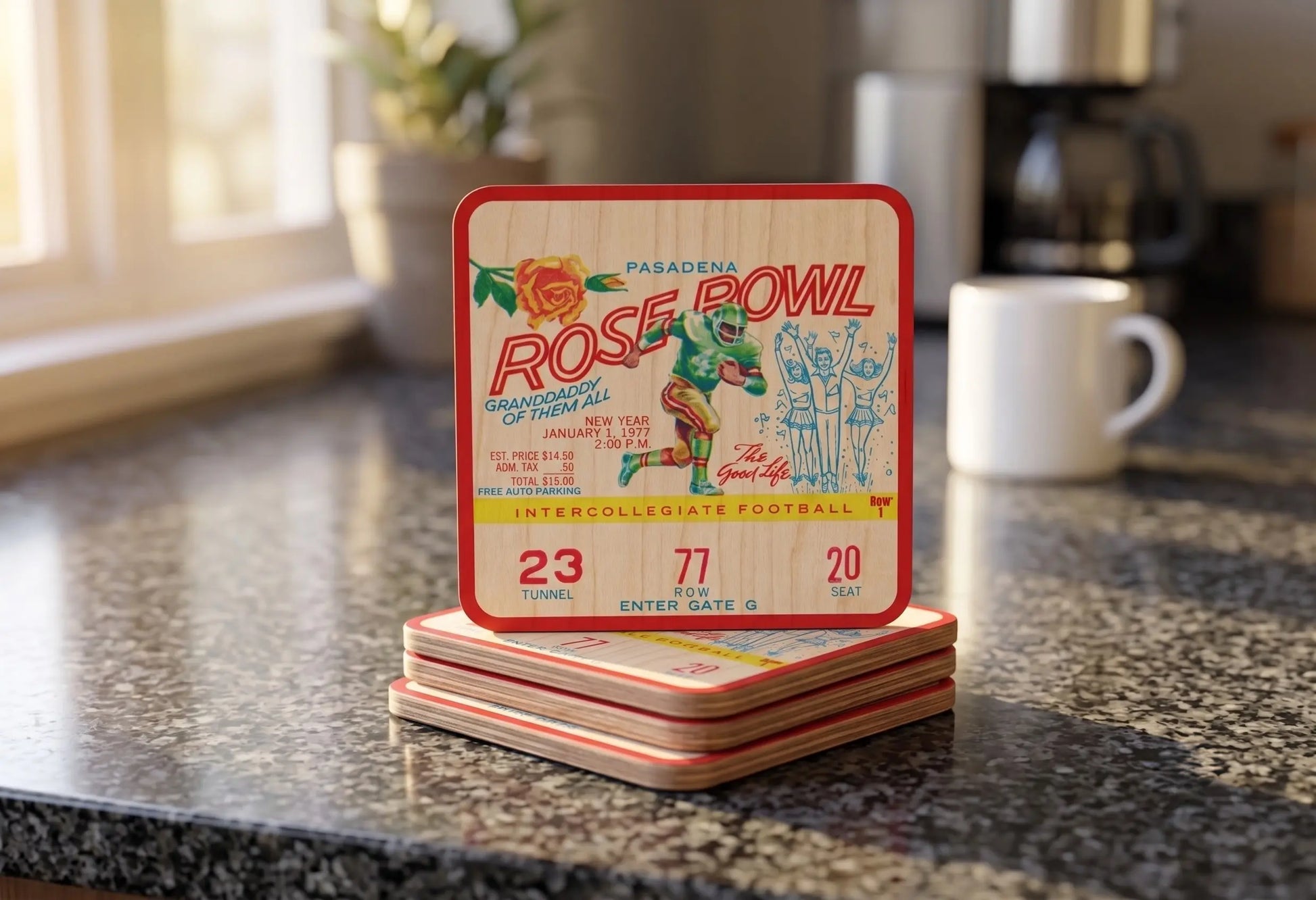 A stack of Row One Brand wooden ticket stub coasters with Row 1 trademark featuring a historic 1977 Pasadena Rose Bowl ticket design, displayed on a dark granite countertop in a kitchen setting.