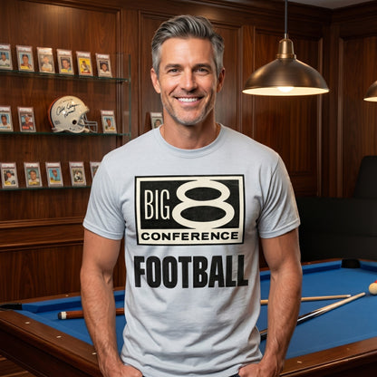 Man wearing a 'Big 8 Conference Football' t-shirt in a room with a pool table and sports memorabilia.