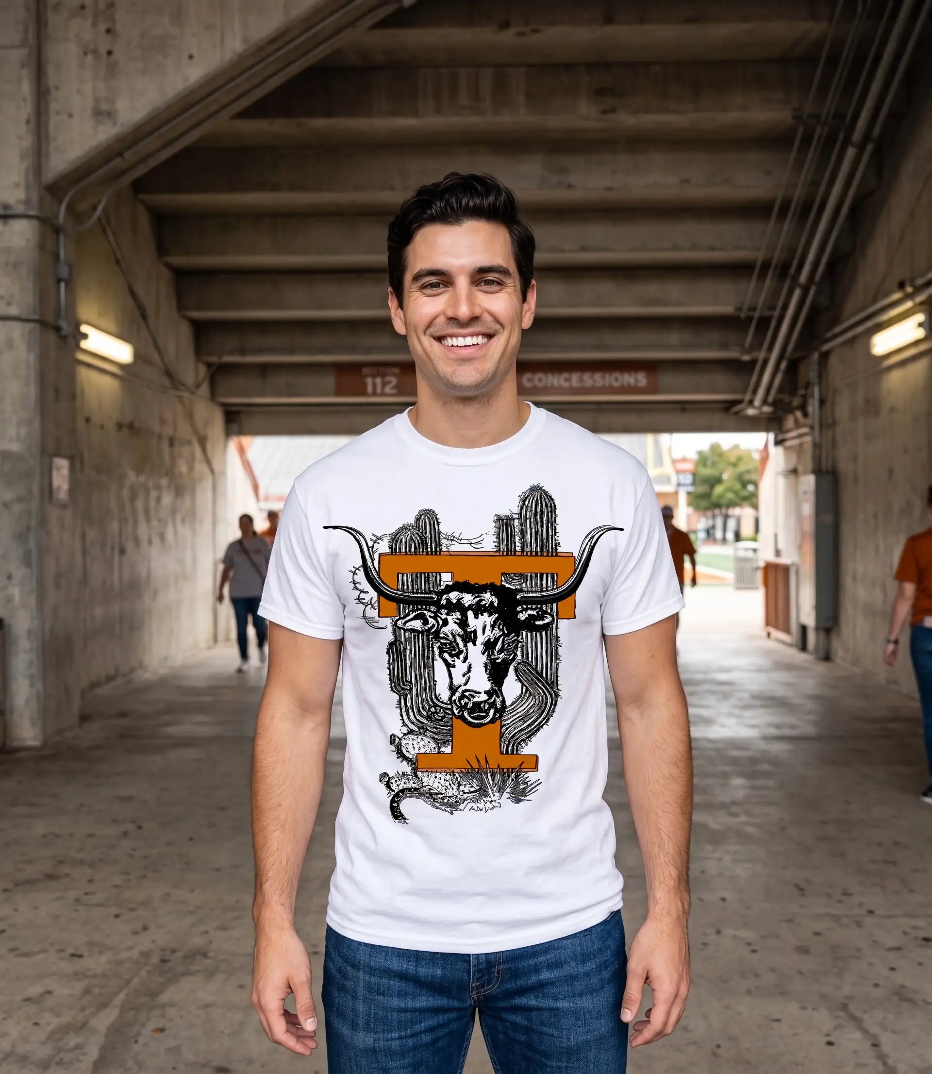 A smiling man wearing a Row One Brand vintage Texas college tee white graphic t-shirt with a longhorn steer and cactus design, standing in a concrete tunnel.