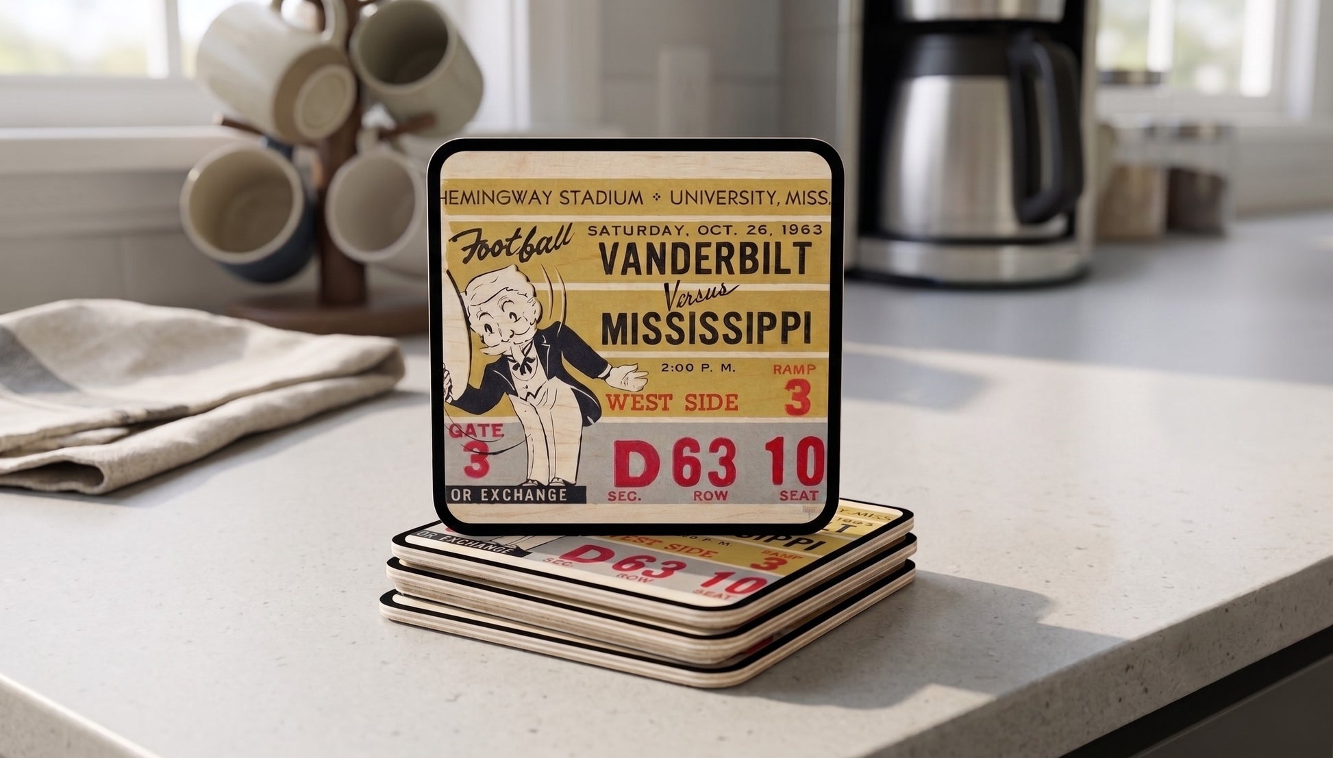 A stack (4) of rectangular birch wood football ticket coasters with rounded corners sits on a kitchen countertop. The top coaster shows a historic 1963 Vanderbilt- Mississippi football ticket design from Row One Brand.